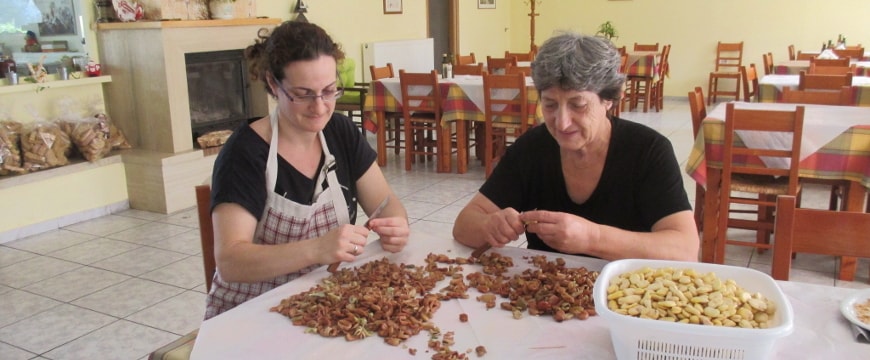 Two women peeling fava beans at a table at Iliomanolis Taverna in Crete