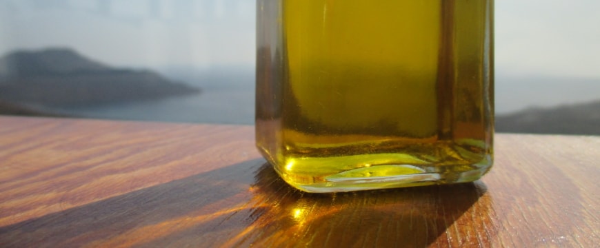 the bottom of a clear glass bottle of olive oil on a wooden table, with a seaview in the distant background
