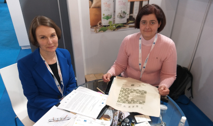 Two women sitting at a table at the Food Expo with a bag and papers related to the LIVINGAGRO project in front of them