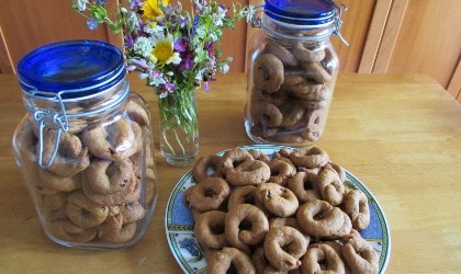 Olive oil orange juice cookies on a plate and in two large jars near a glass of wildflowers