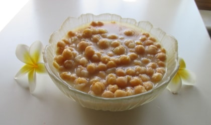 chickpeas in a glass bowl with yellow and white plumeria flowers next to it