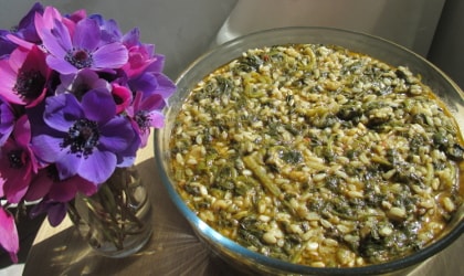 a large glass bowl of spanakorizo next to a small bouquet of anemones