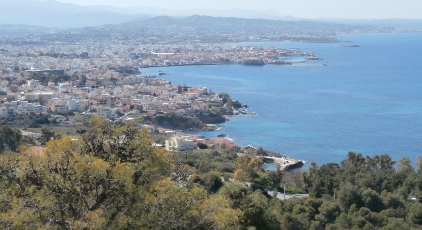 City of Chania viewed from a hill above it, with olive groves in front right and sea on the right