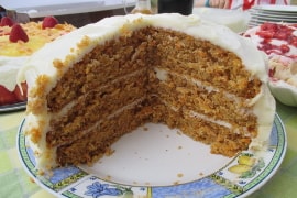 three layer carrot cake with cream cheese icing, with a big wedge cut out of it