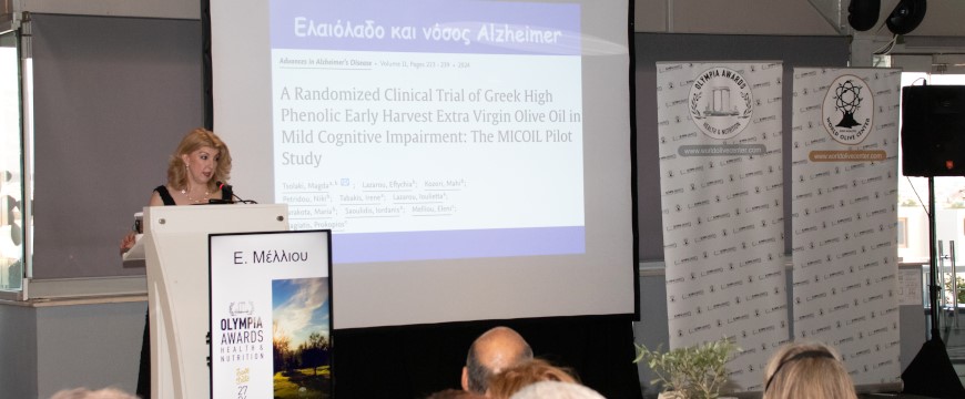 Dr. Eleni Melliou presenting at the Olympia Awards ceremony, with a slide behind her about a study of high phenolic olive oil in patients with mild cognitive impairment