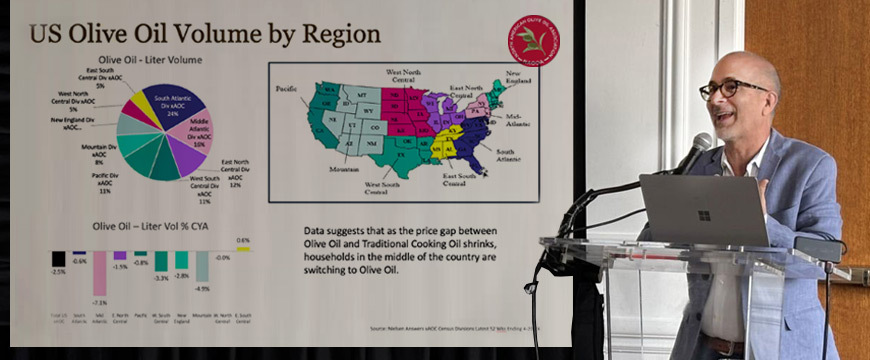 NAOOA executive director Joseph Profaci giving a speech, with a screen near him showing US Olive Oil Volume By Region with graphs and a map