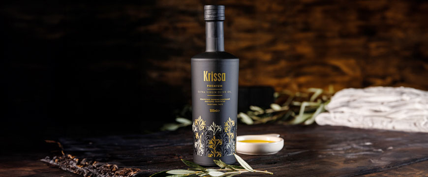 a black bottle of Krissa extra virgin olive oil on a wooden table with a brown and black background