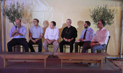 six men sitting on chairs in a row on a small stage to discuss conference conclusions