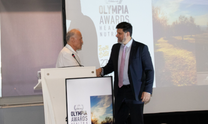 Dr. Georgios Spanoudis shaking hands with Dr. Prokopis Magiatis by the podium at the Olympia Health and Nutrition Awards