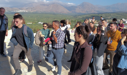 Cretan Lifestyle Conference participants entering a winery, with olive groves and hills in the background