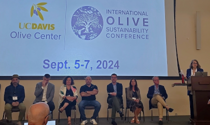 panel members sitting below a large screen displaying the conference and Olive Center names and logos