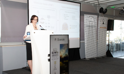 Dr. Pavlina Sverak presenting scientific work at a podium, with a screen behind her and Olympia Awards and World Olive Center logos nearby